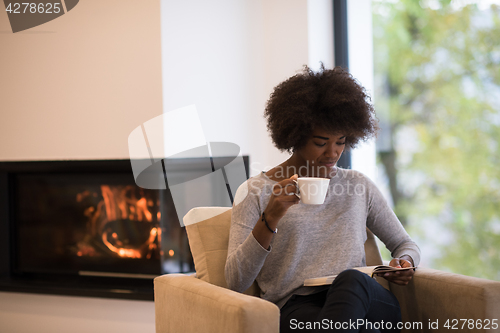 Image of black woman reading book  in front of fireplace