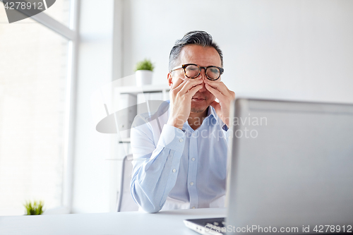 Image of tired businessman in glasses with laptop at office
