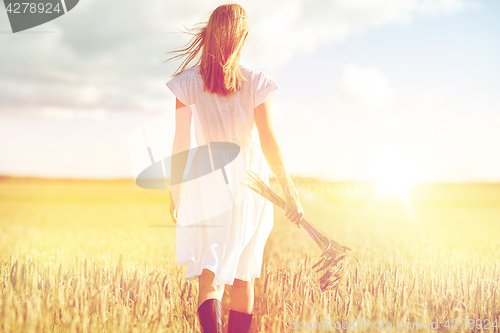 Image of young woman with cereal spikelets walking on field