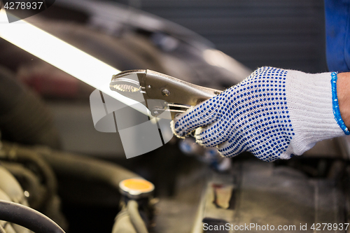 Image of mechanic man with pliers repairing car at workshop