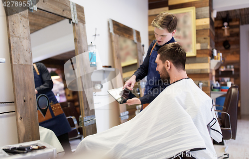 Image of barber showing tablet pc to man at barbershop