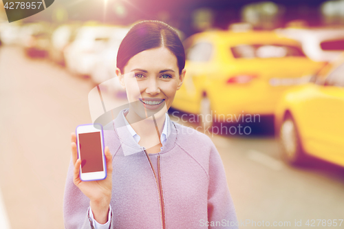 Image of smiling woman showing smartphone over taxi in city