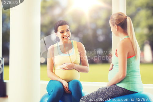 Image of two happy pregnant women sitting on balls in gym