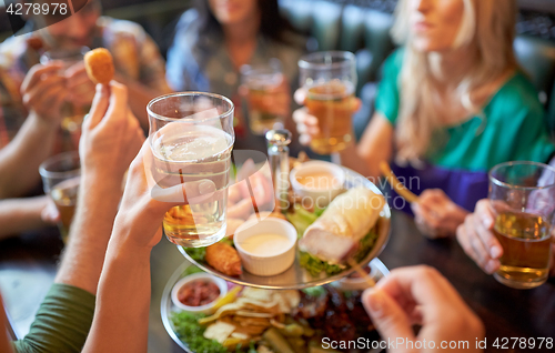 Image of happy friends eating and drinking at bar or pub