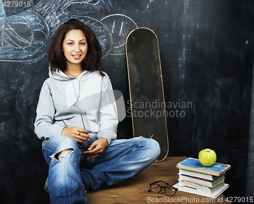 Image of young cute teenage girl in classroom at blackboard seating on ta