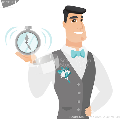 Image of Young caucasian groom holding alarm clock.