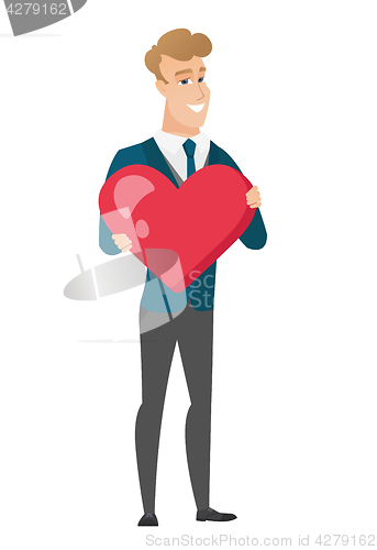 Image of Caucasian groom holding a big red heart.