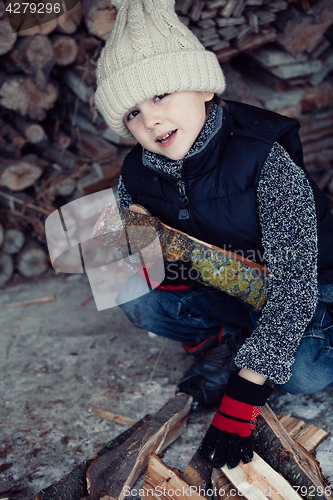 Image of Little boy chopping firewood in the front yard at the day time.