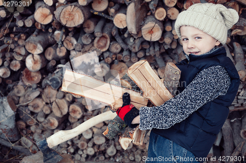 Image of Little boy chopping firewood in the front yard at the day time.