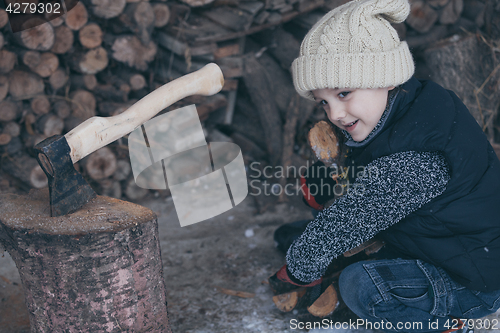 Image of Little boy chopping firewood in the front yard at the day time.