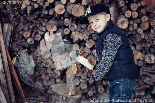 Image of Little boy chopping firewood in the front yard at the day time.