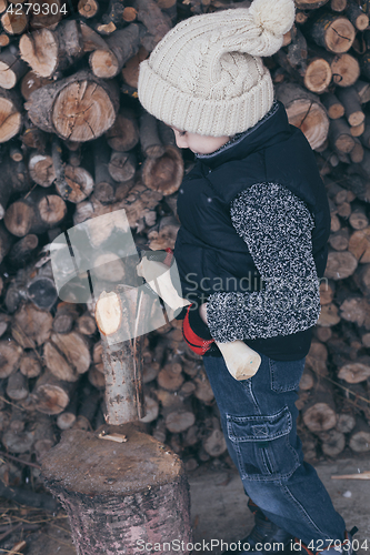 Image of Little boy chopping firewood in the front yard at the day time.