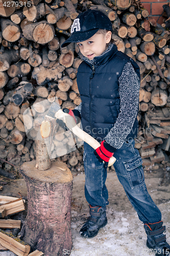 Image of Little boy chopping firewood in the front yard at the day time.