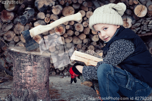 Image of Little boy chopping firewood in the front yard at the day time.