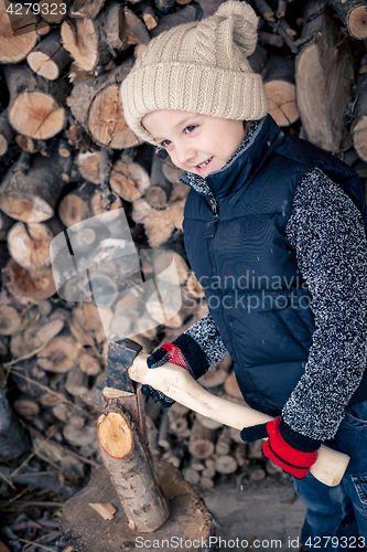 Image of Little boy chopping firewood in the front yard at the day time.