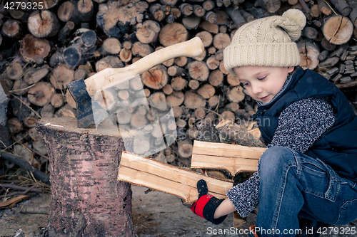 Image of Little boy chopping firewood in the front yard at the day time.