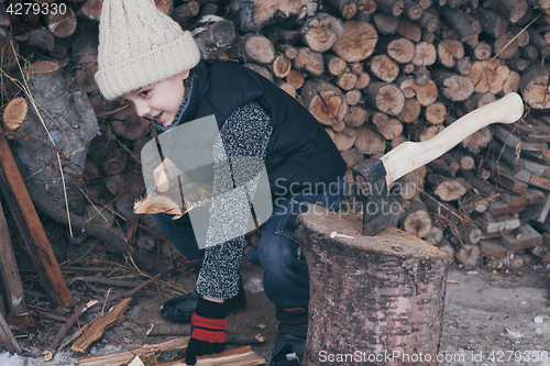 Image of Little boy chopping firewood in the front yard at the day time.