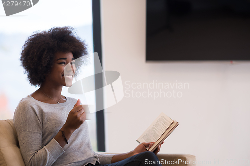 Image of black woman reading book  in front of fireplace