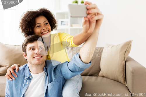 Image of happy couple with smartphone taking selfie at home