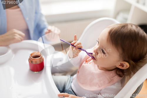 Image of baby girl with spoon eating puree from jar at home