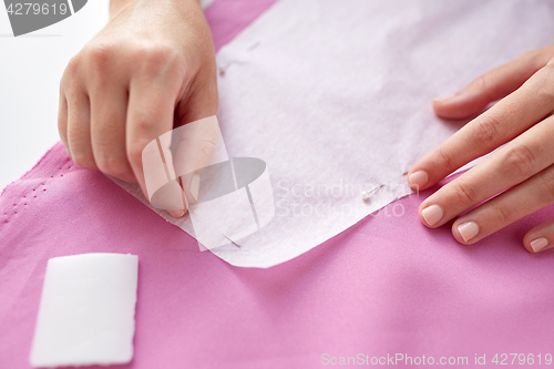 Image of woman with pins stitching paper pattern to fabric