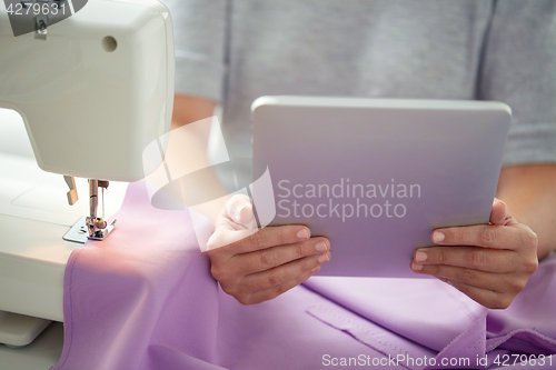 Image of tailor with sewing machine, tablet pc and fabric