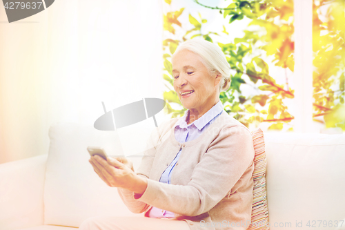 Image of senior woman with smartphone texting at home