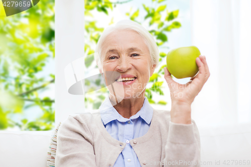 Image of happy senior woman with green apple at home