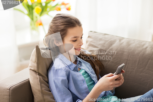 Image of smiling girl texting on smartphone at home