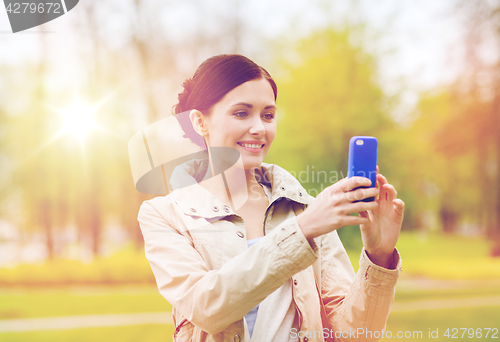 Image of smiling woman taking picture with smartphone