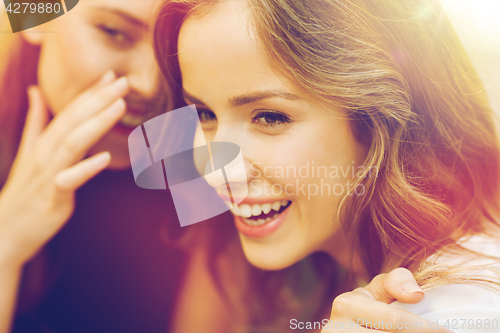 Image of smiling young women gossiping and whispering