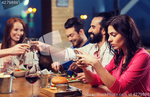 Image of woman with smartphone and friends at restaurant