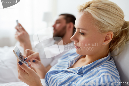 Image of couple with smartphones in bed at home