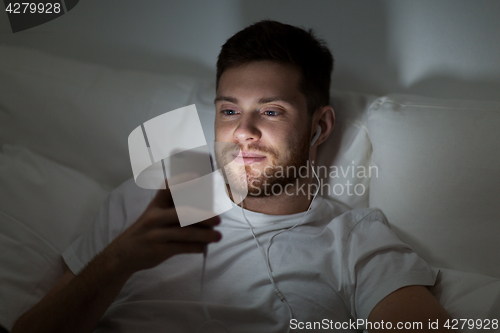 Image of man with smartphone and earphones in bed at night