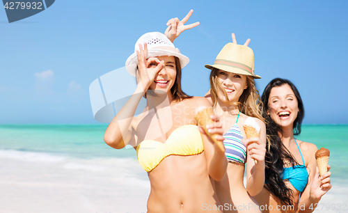 Image of group of smiling women eating ice cream on beach