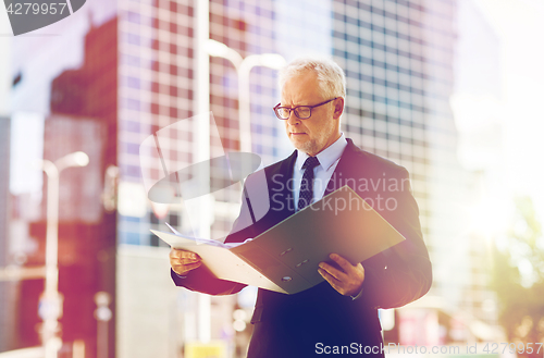 Image of senior businessman with ring binder folder in city