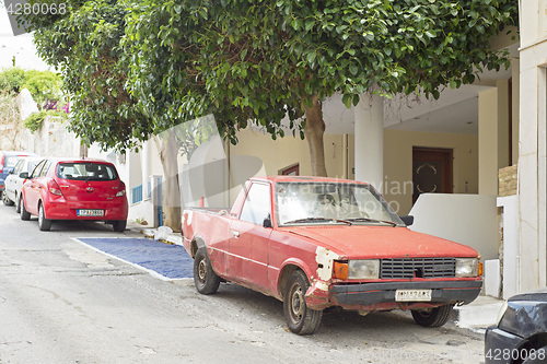 Image of Old rusty red car standing in the street
