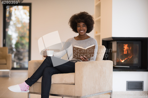 Image of black woman reading book  in front of fireplace