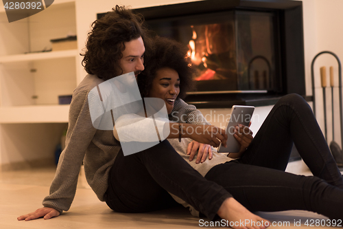 Image of multiethnic couple using tablet computer on the floor