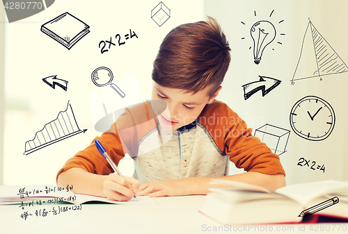 Image of smiling student boy writing to notebook at home