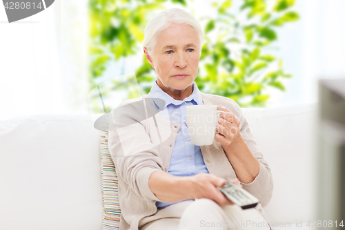 Image of senior woman watching tv and drinking tea at home