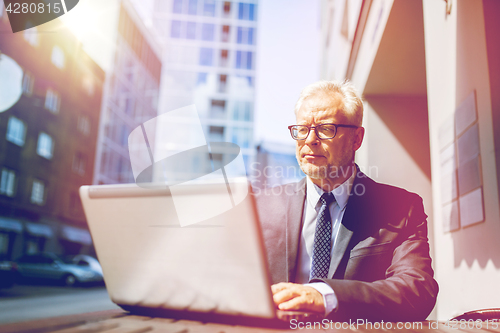 Image of senior businessman with laptop at city street cafe