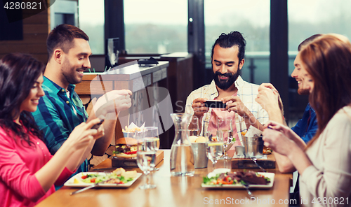 Image of happy friends taking picture of food at restaurant