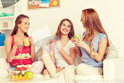 Image of happy young women drinking tea with sweets at home