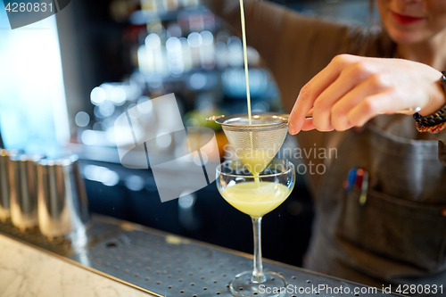 Image of bartender pouring cocktail into glass at bar