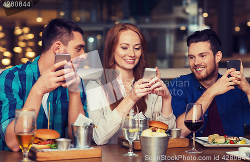 Image of happy friends with smartphones at restaurant
