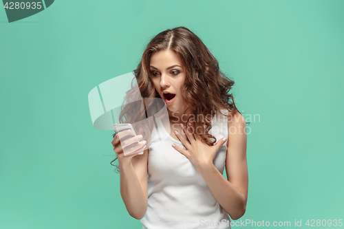 Image of Shocked woman looking at mobile phone on green background