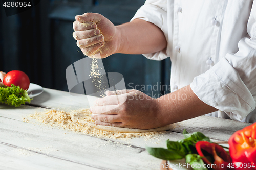 Image of Closeup hand of chef baker in white uniform making pizza at kitchen