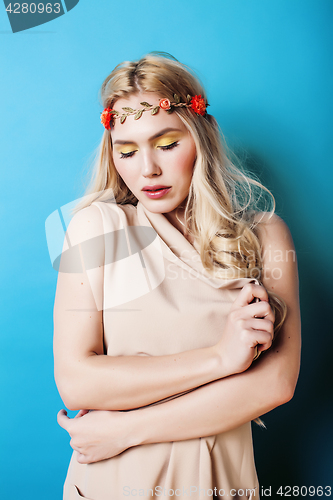 Image of young pretty blond girl with curly blond hair and little lowers happy smiling on blue sky background, lifestyle people concept