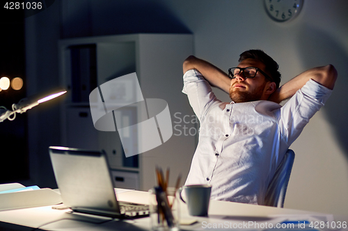 Image of man with laptop stretching at night office